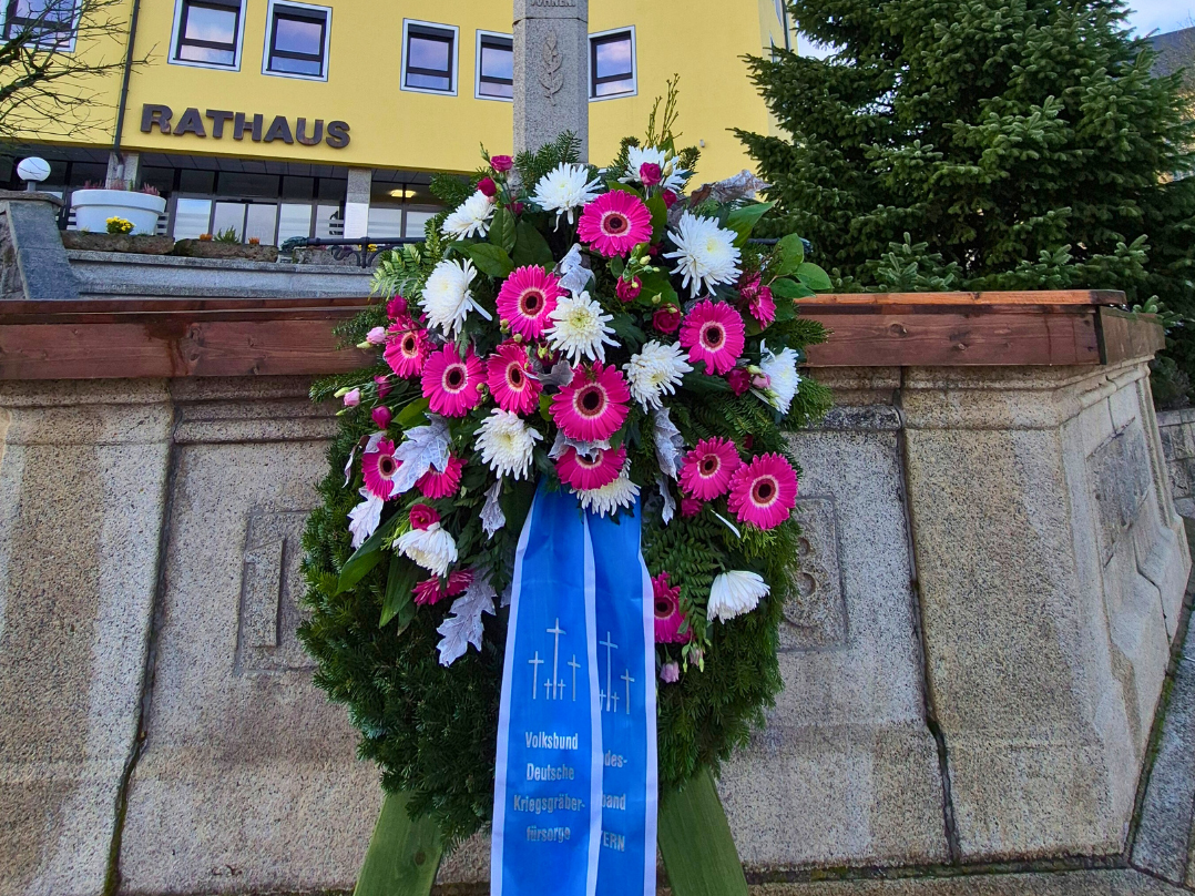 Ein mit rosa und weißen Blüten gestalteter Kranz steht am Rathausbrunnen zum Volkstrauertag.