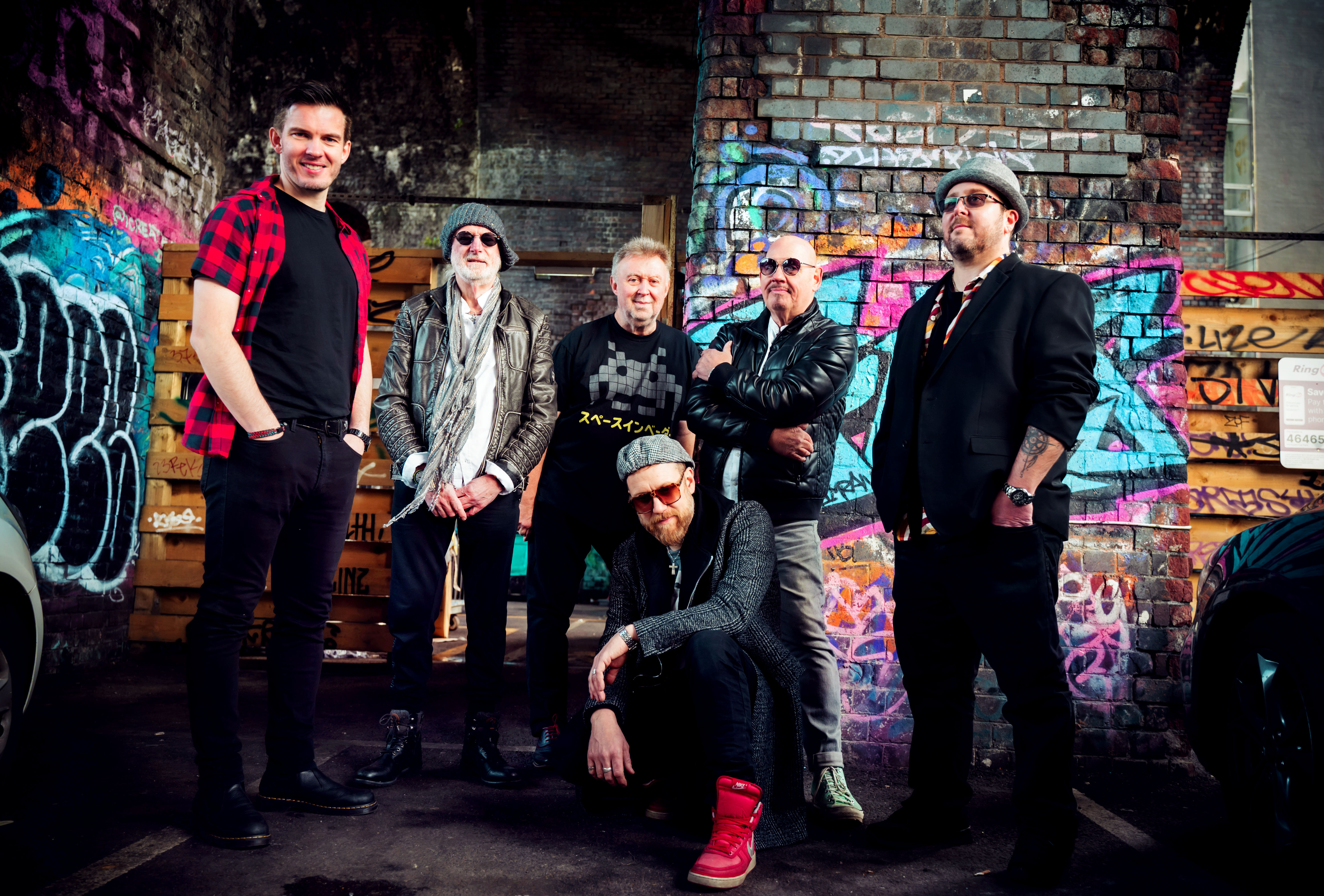 Climax Blues Band Die sechsköpfige Climax Blues Band auf einem Gruppenfoto unter einer Unterführung, deren gemauerten Wände mit Graffiti besprüht sind.