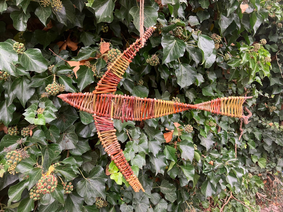 Weidenvogel Ein aus Weidenästen geflochtener Vogel vor einer grünen Hecke