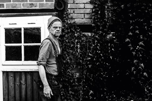 Tom Liwa Der Singer-Songwriter abgelichtet vor einer Hausfassade mit Fenster und Begrünung im Hintergrund. Das Bild ist schwarz-weiß
